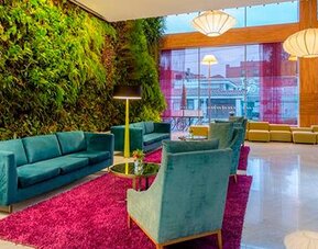 Contemporary lounge with teal sofas, colourful armchairs, magenta rug and vertical garden at Sonesta Hotel Bogotá.