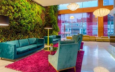 Contemporary lounge with teal sofas, colourful armchairs, magenta rug and vertical garden at Sonesta Hotel Bogotá.
