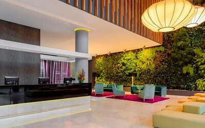 Reception area with dark front desk, green living wall, orange seating and decorative pendant lights at Sonesta Hotel Bogotá.