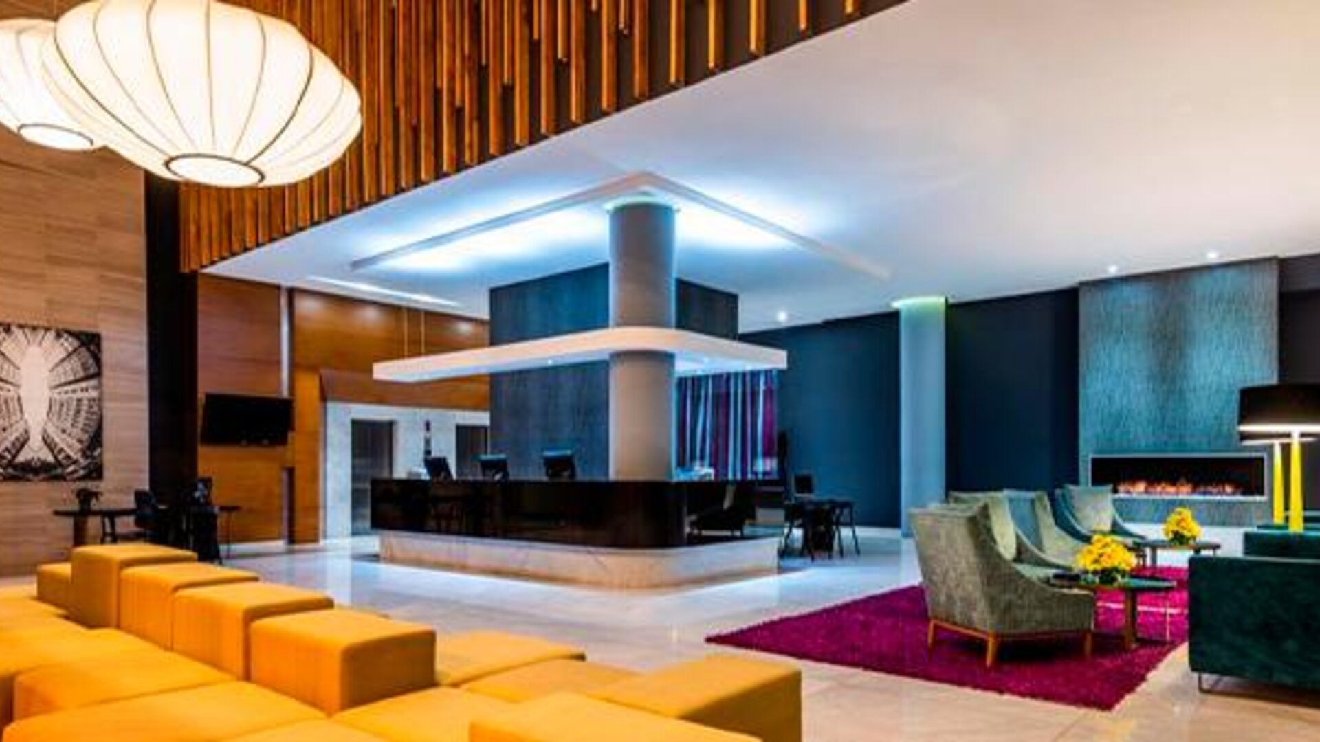 Hotel lobby with reception desk, orange lounge seating, wood accents and contemporary pendant lights at Sonesta Hotel Bogotá.