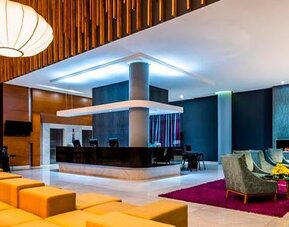 Hotel lobby with reception desk, orange lounge seating, wood accents and contemporary pendant lights at Sonesta Hotel Bogotá.