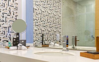 Bathroom vanity with white countertop, round vessel sink, mirror and geometric-patterned wall tiles at Sonesta Hotel Bogotá.