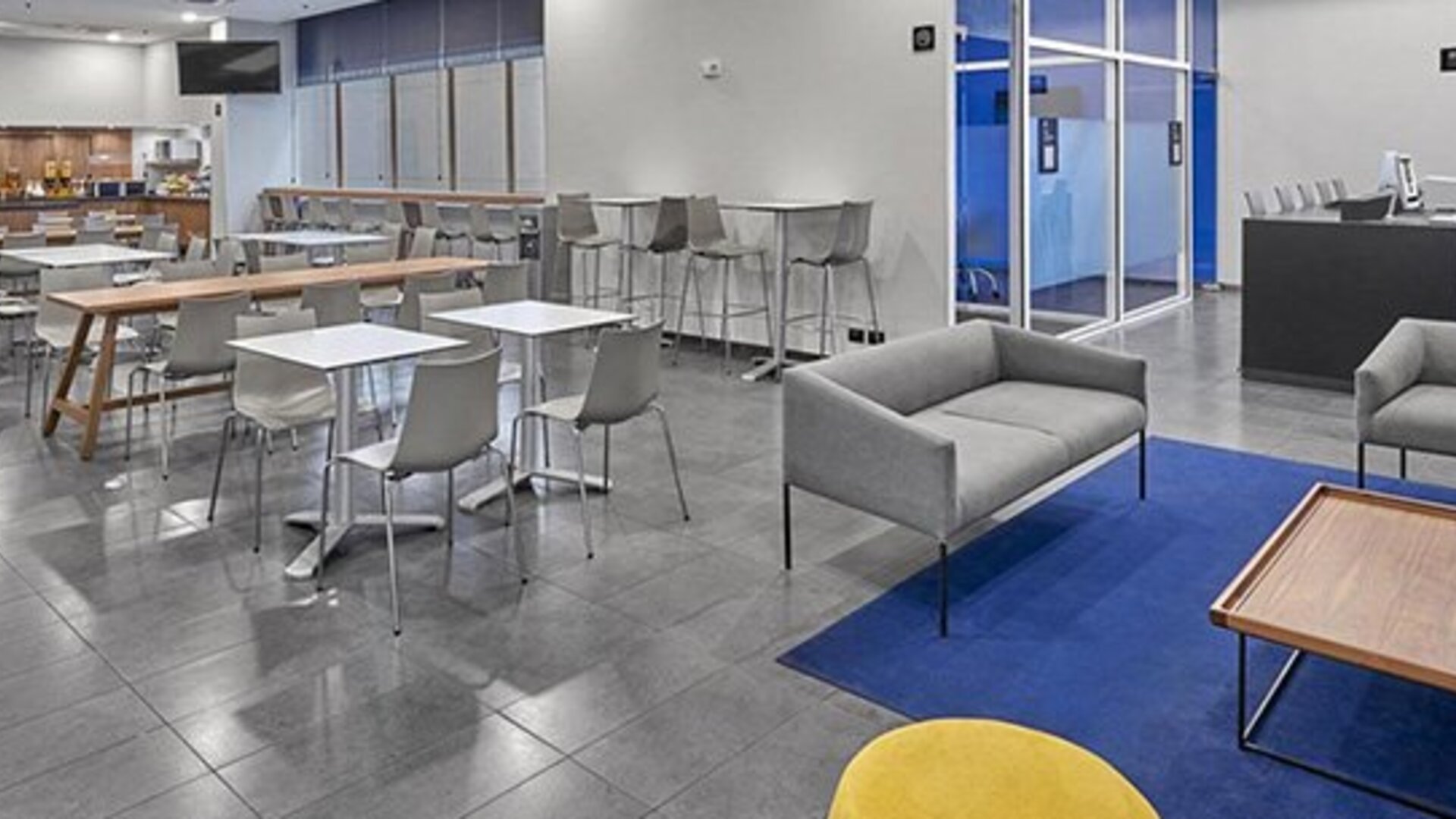Hotel dining area with communal tables, grey chairs, blue carpet and lounge seating at City Express by Marriott CDMX La Villa.