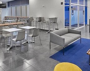 Hotel dining area with communal tables, grey chairs, blue carpet and lounge seating at City Express by Marriott CDMX La Villa.