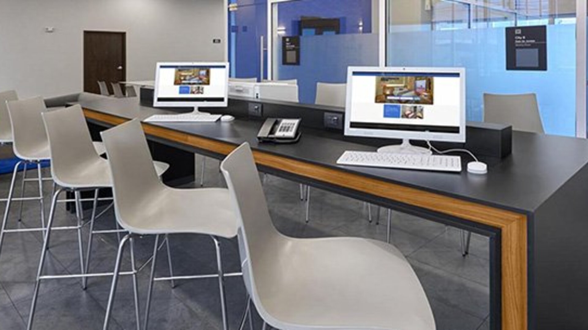 Business centre with desktop computers, white chairs and a long counter beside floor-to-ceiling windows at City Express by Marriott CDMX La Villa.