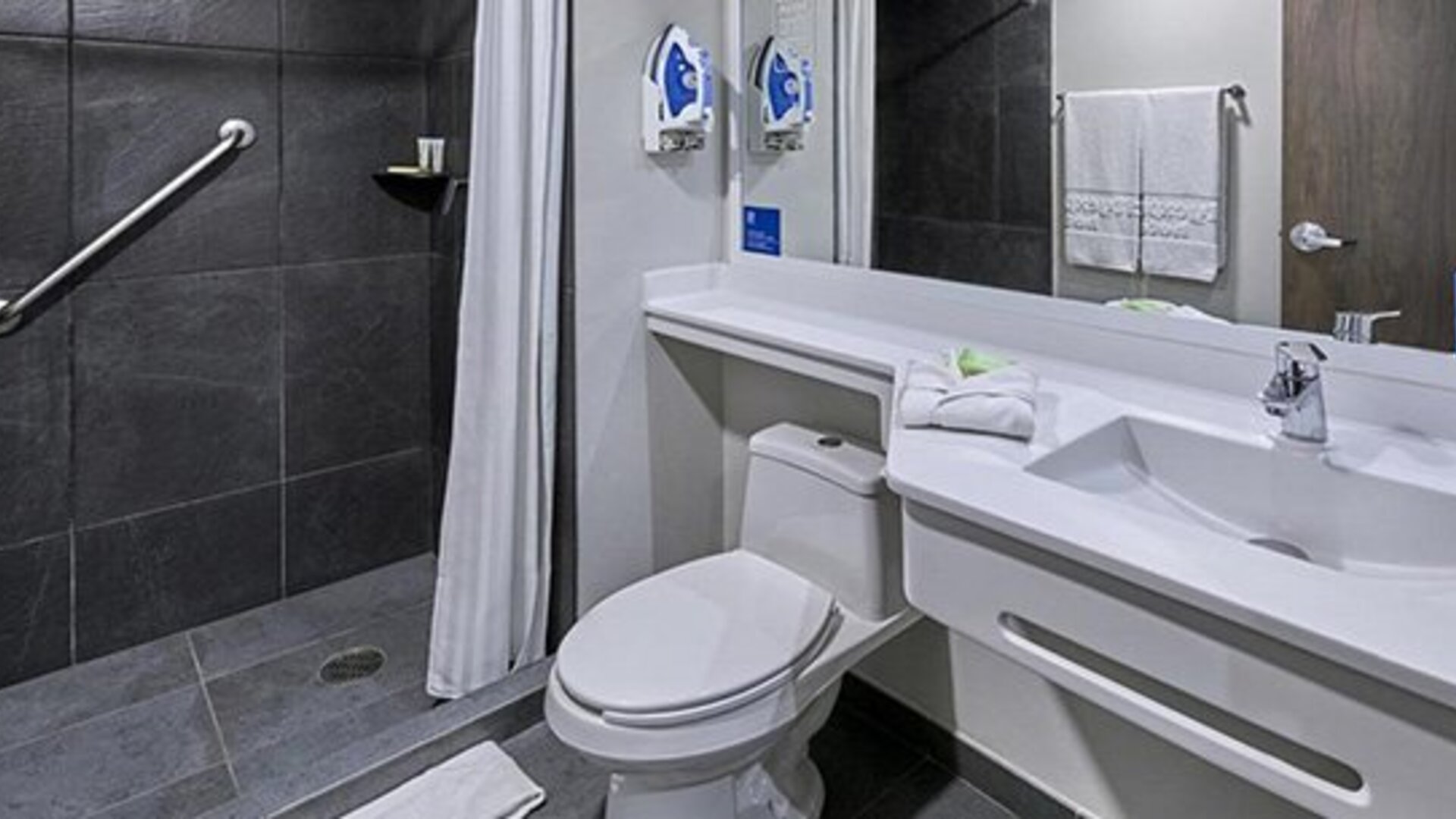 Accessible bathroom with grab bar, roll-in shower, toilet, white vanity and wall-mounted mirror at City Express by Marriott CDMX La Villa.