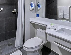 Accessible bathroom with grab bar, roll-in shower, toilet, white vanity and wall-mounted mirror at City Express by Marriott CDMX La Villa.