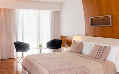 Guest room with king-size bed, neutral bedding, wooden accent wall, bedside tables and seating area at Design Suites Buenos Aires.