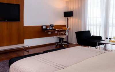 Guest room with large bed, wall-mounted television, desk, black lounge chairs and floor-to-ceiling curtains at Design Suites Buenos Aires.