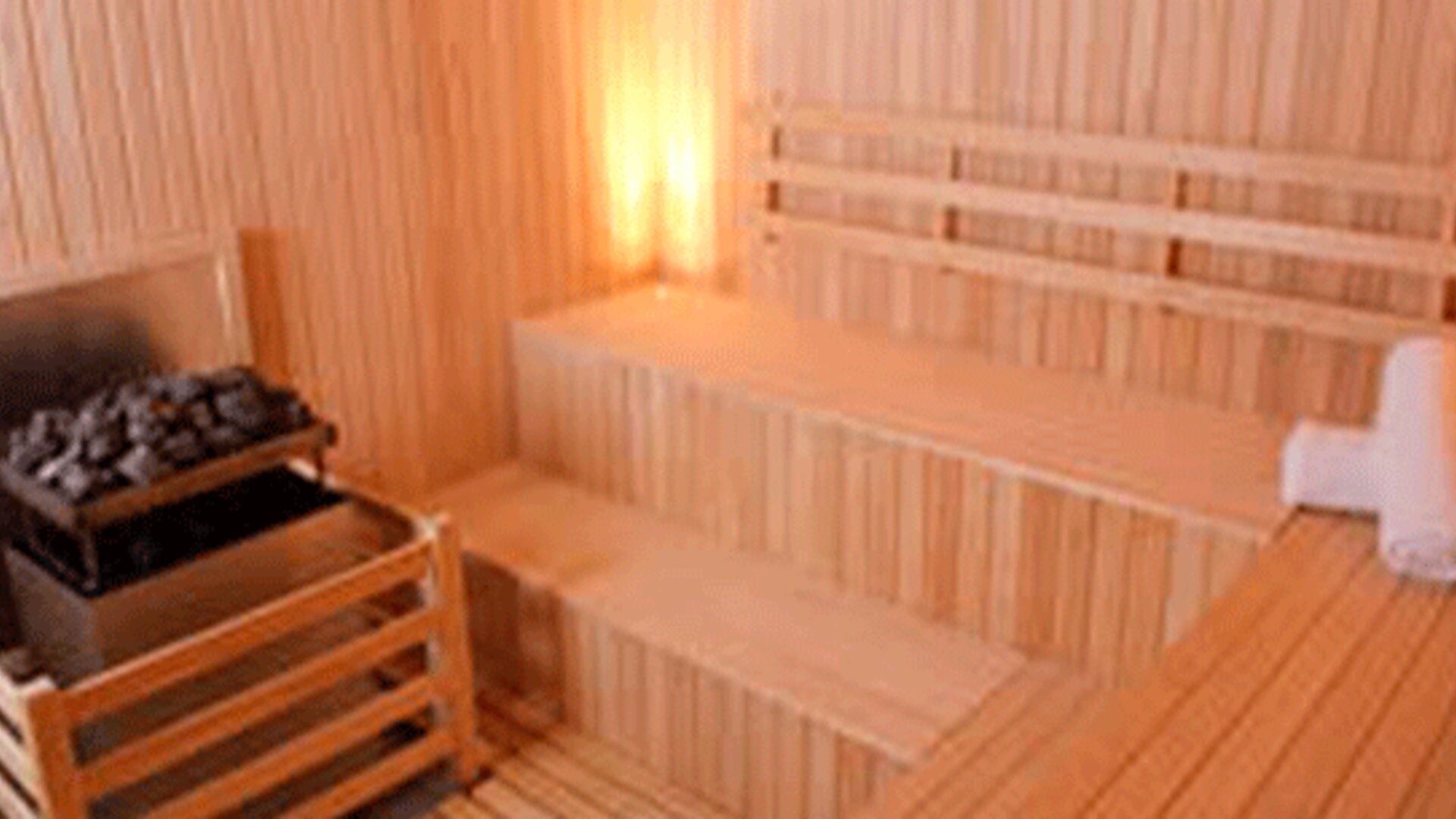Wooden sauna with tiered benches, stone heater and folded white towels at Design Suites Buenos Aires.