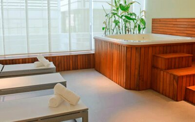 Spa relaxation area with white loungers, rolled towels, wooden hot tub and large windows at Design Suites Buenos Aires.
