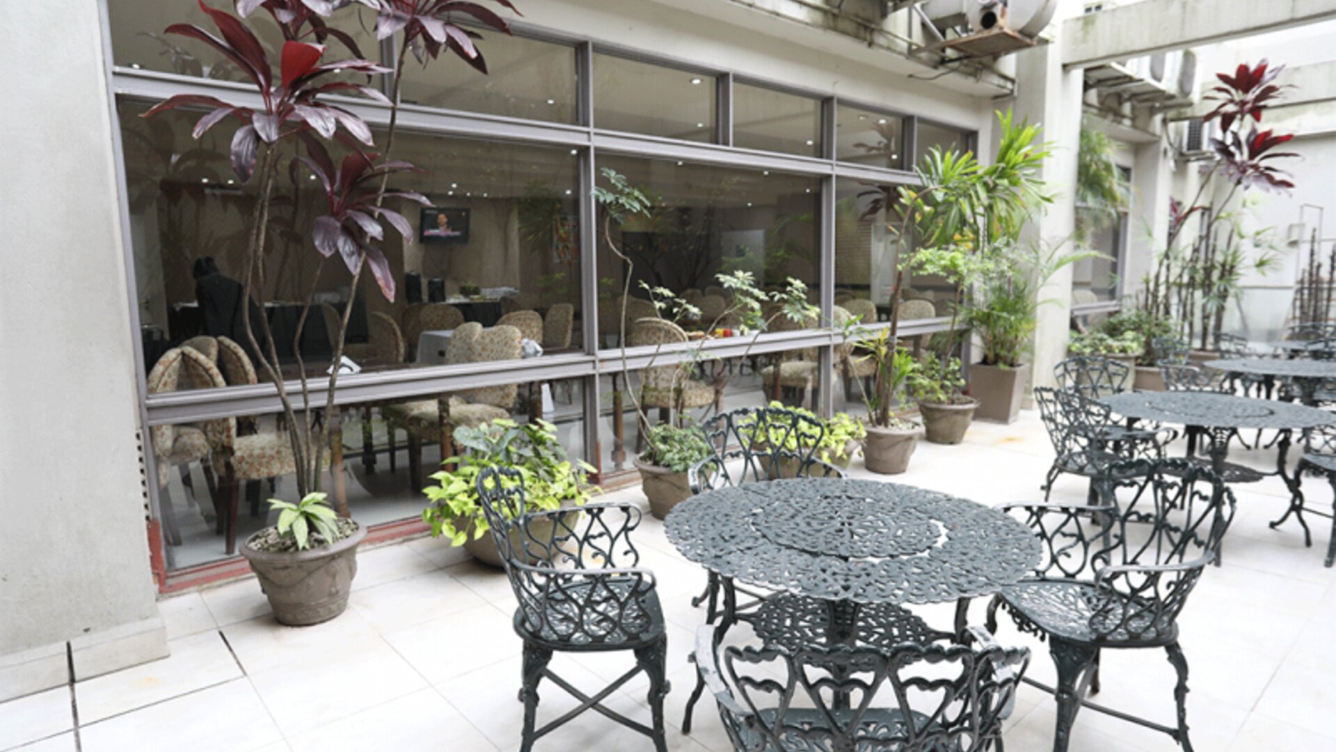 Outdoor terrace with decorative black metal tables and chairs beside large windows and potted plants at HR Esmeralda Luxor.