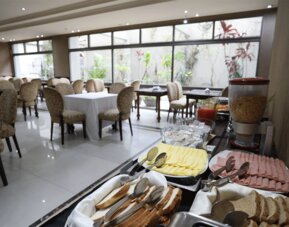 Breakfast buffet displaying sliced cheese, cold meats, bread and cereal beside dining tables at HR Esmeralda Luxor.
