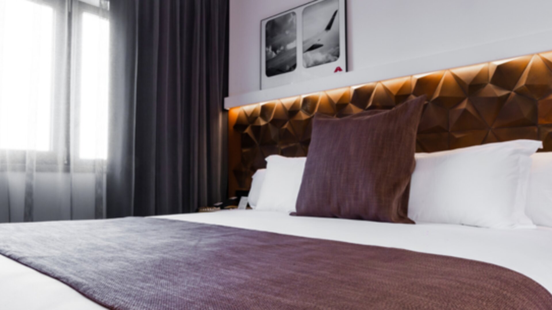 Close view of a king bed with white bedding, brown runner, decorative cushions and illuminated geometric headboard at Hotel Best Western PLUS Alfa Aeropuerto.