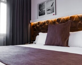 Close view of a king bed with white bedding, brown runner, decorative cushions and illuminated geometric headboard at Hotel Best Western PLUS Alfa Aeropuerto.