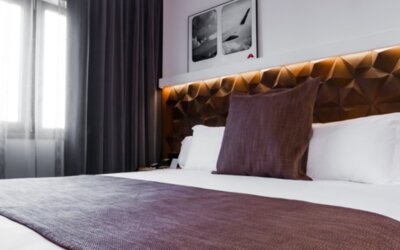 Close view of a king bed with white bedding, brown runner, decorative cushions and illuminated geometric headboard at Hotel Best Western PLUS Alfa Aeropuerto.