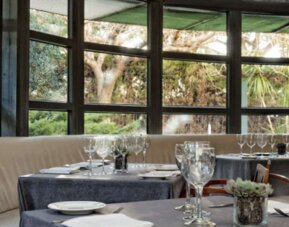 Restaurant seating area with tables, white tablecloths, glass partitions and views of the surrounding garden at Hotel Best Western PLUS Alfa Aeropuerto.