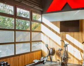Gym with treadmill, stationary bikes, weight bench and dumbbells in a wood-panelled room at Hotel Best Western PLUS Alfa Aeropuerto.