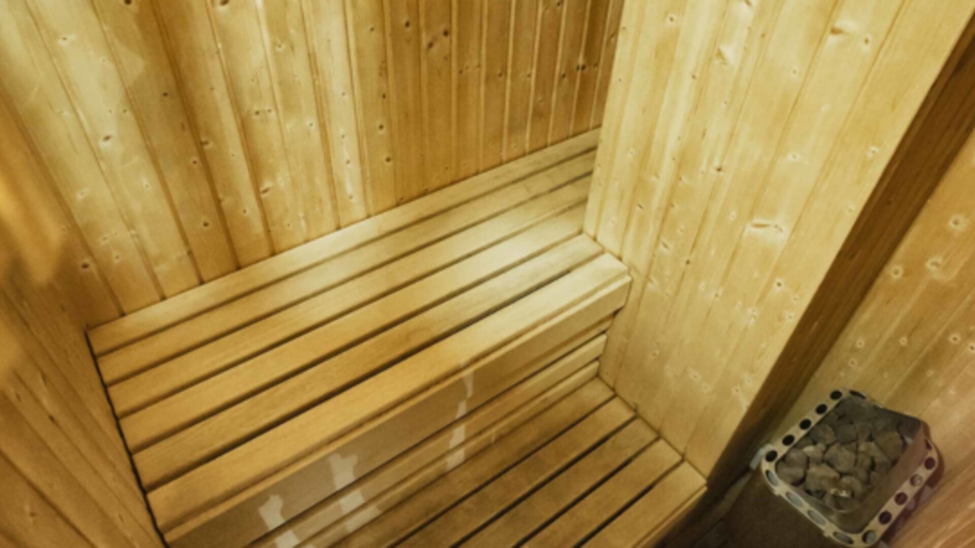 Wooden sauna with tiered benches and a stone heater in the corner at Hotel Best Western PLUS Alfa Aeropuerto.