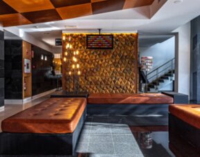 Hotel lobby with brown leather seating, geometric feature wall, staircase and large windows overlooking greenery at Hotel Best Western PLUS Alfa Aeropuerto.
