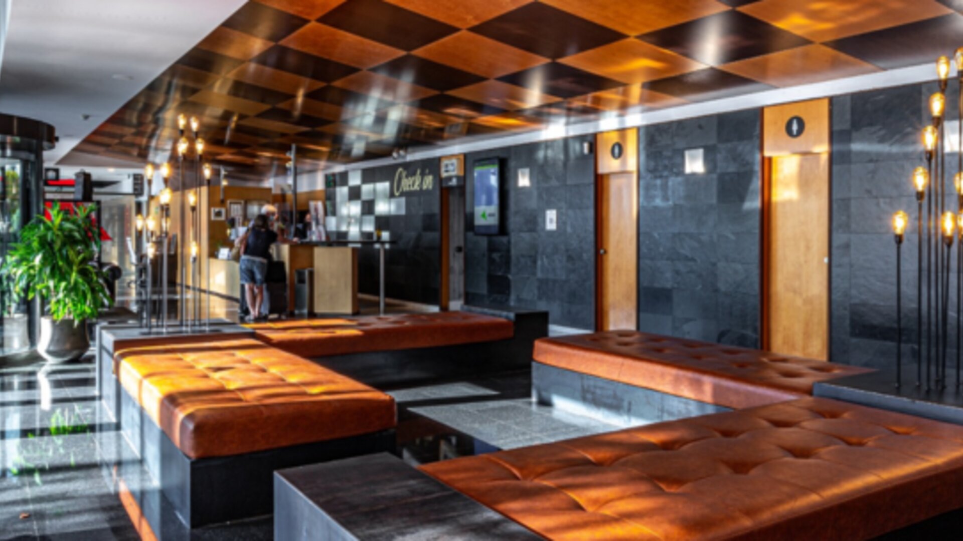 Lobby lounge with brown leather benches, dark stone walls, illuminated decorative lighting and a revolving entrance at Hotel Best Western PLUS Alfa Aeropuerto.