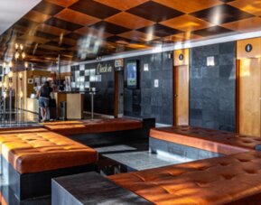 Lobby lounge with brown leather benches, dark stone walls, illuminated decorative lighting and a revolving entrance at Hotel Best Western PLUS Alfa Aeropuerto.