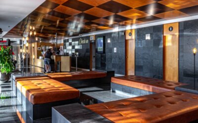 Lobby lounge with brown leather benches, dark stone walls, illuminated decorative lighting and a revolving entrance at Hotel Best Western PLUS Alfa Aeropuerto.