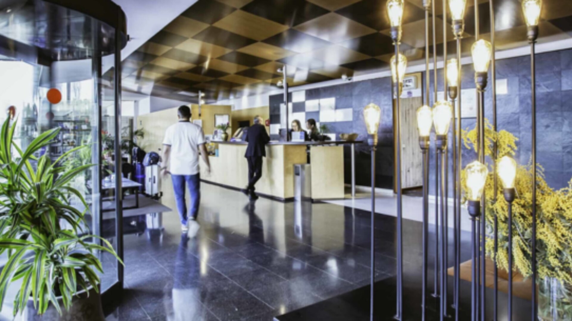 Hotel reception area with front desk, dark stone walls, decorative pendant lights and a glass revolving door at Hotel Best Western PLUS Alfa Aeropuerto.
