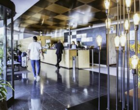 Hotel reception area with front desk, dark stone walls, decorative pendant lights and a glass revolving door at Hotel Best Western PLUS Alfa Aeropuerto.