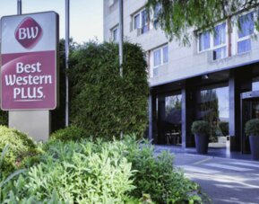 Modern hotel exterior with Best Western PLUS signage, glass entrance and landscaped greenery at Hotel Best Western PLUS Alfa Aeropuerto.