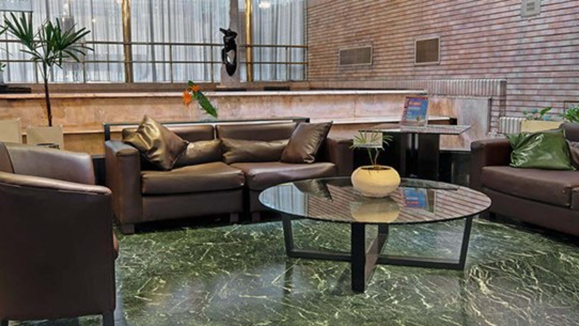 Lounge with dark leather sofas, armchairs, glass coffee table and green marble flooring at Hotel Regente Palace.