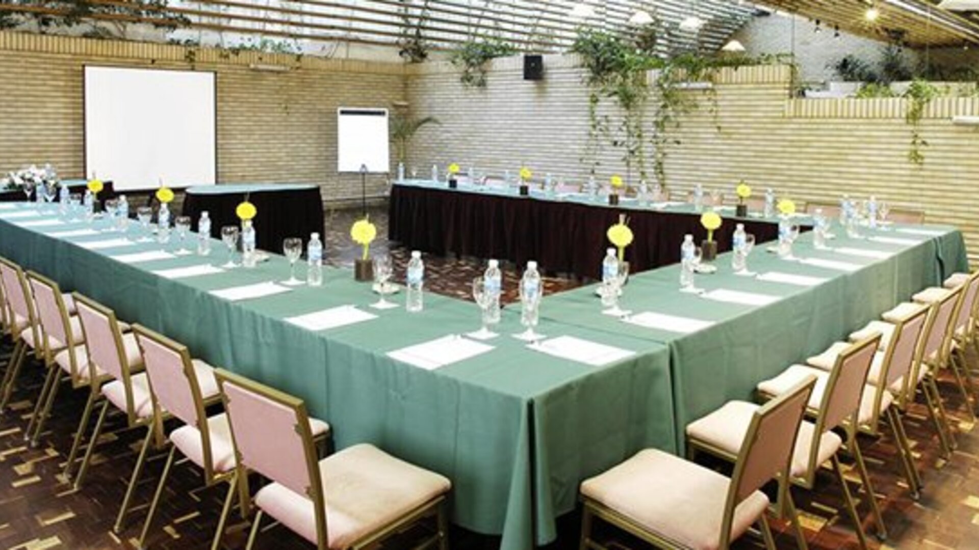 Conference room with green-covered tables arranged in a U-shape, chairs, place settings and projection screens at Hotel Regente Palace.