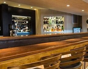 Long wooden bar counter lined with stools, backed by shelves of wine bottles and drinks at Hotel Regente Palace.