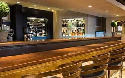 Long wooden bar counter lined with stools, backed by shelves of wine bottles and drinks at Hotel Regente Palace.