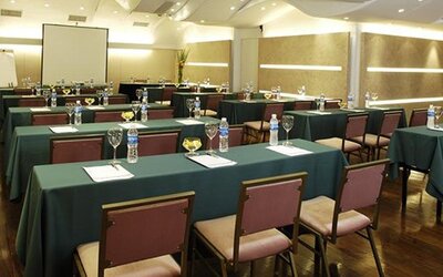Meeting room arranged with green tablecloths, rows of chairs, water bottles and a projection screen at Hotel Regente Palace.