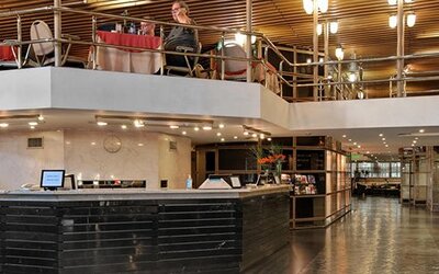 Hotel reception with black front desk, upper-level dining area, metal railings and wooden slat ceiling at Hotel Regente Palace.
