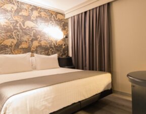 King bed with white linens, grey runner, patterned decorative headboard and warm bedside lights at Hotel Silken Saaj Las Palmas.