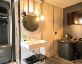 Guest room workspace with wooden desk, chair, wall-mounted television and open wardrobe beside the bathroom at Hotel Silken Saaj Las Palmas.