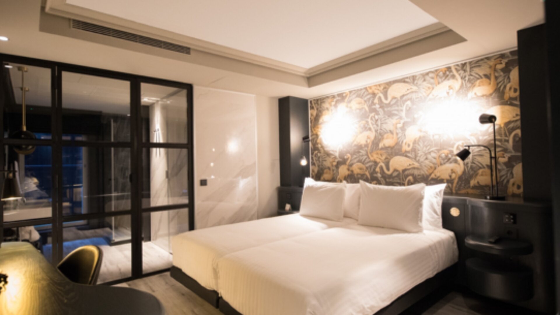 Guest room with white bed, patterned feature wall, bedside lighting and black-framed glass doors at Hotel Silken Saaj Las Palmas.