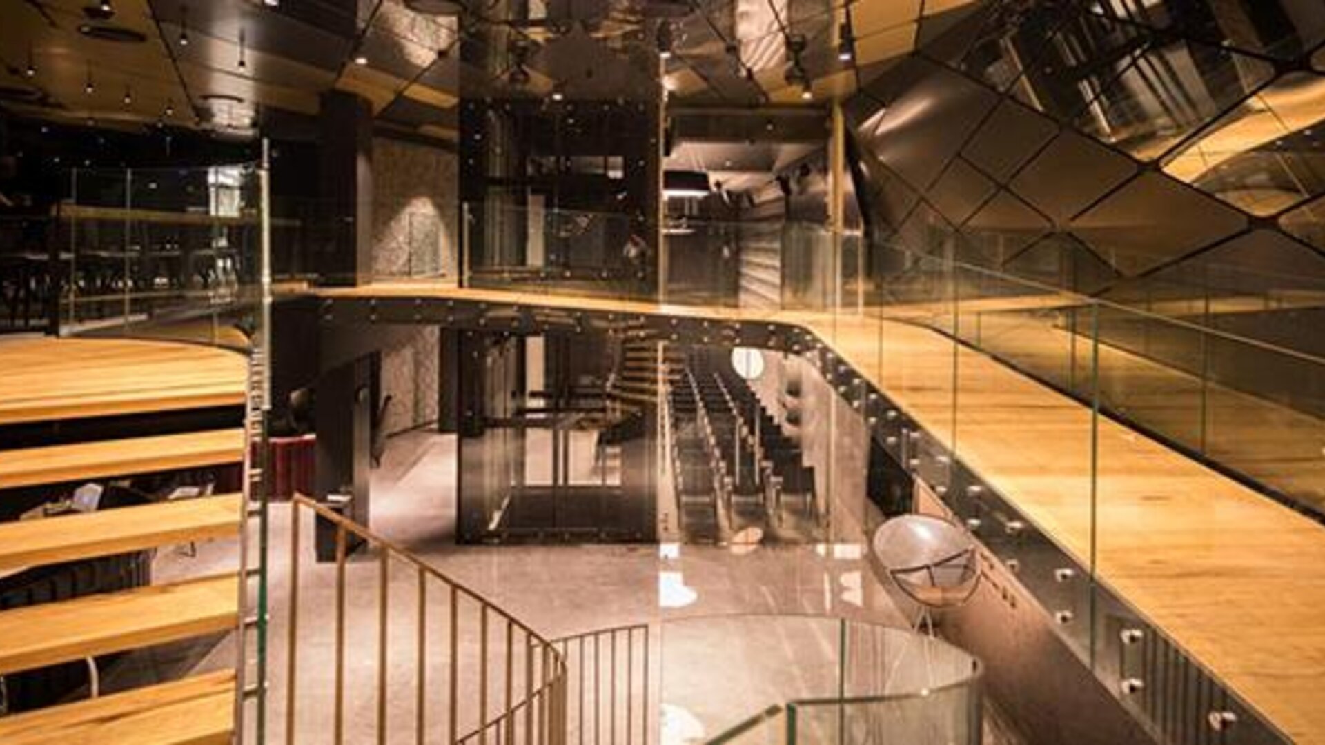Contemporary multi-level interior with wooden tiered seating, glass railings and angular reflective ceiling panels at Hotel Silken Saaj Las Palmas.