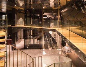Contemporary multi-level interior with wooden tiered seating, glass railings and angular reflective ceiling panels at Hotel Silken Saaj Las Palmas.