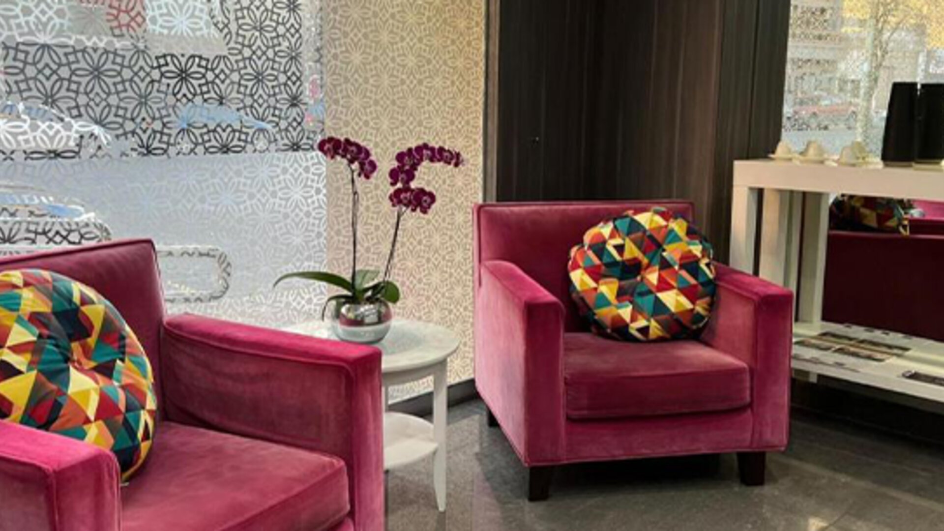 Lobby lounge with magenta armchairs, colourful cushions, purple orchids and patterned decorative panels at Ian Hotel.