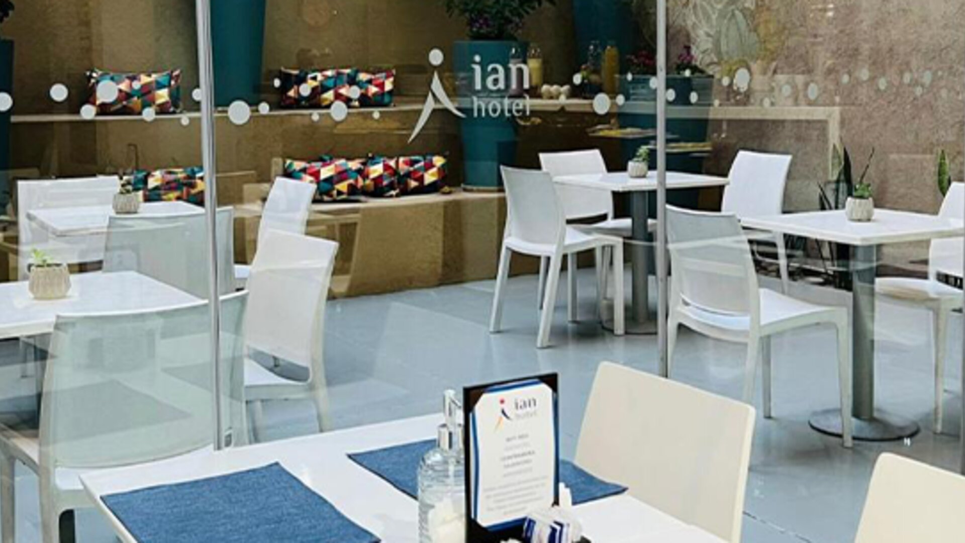 Dining area with white tables, chairs, blue placemats and glass doors overlooking a courtyard at Ian Hotel.