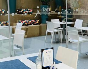 Dining area with white tables, chairs, blue placemats and glass doors overlooking a courtyard at Ian Hotel.