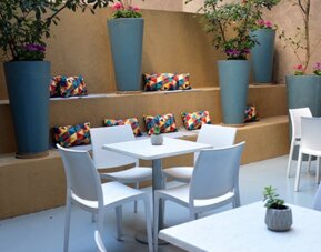 Outdoor dining patio with white tables and chairs, tall blue planters and colourful cushions at Ian Hotel.