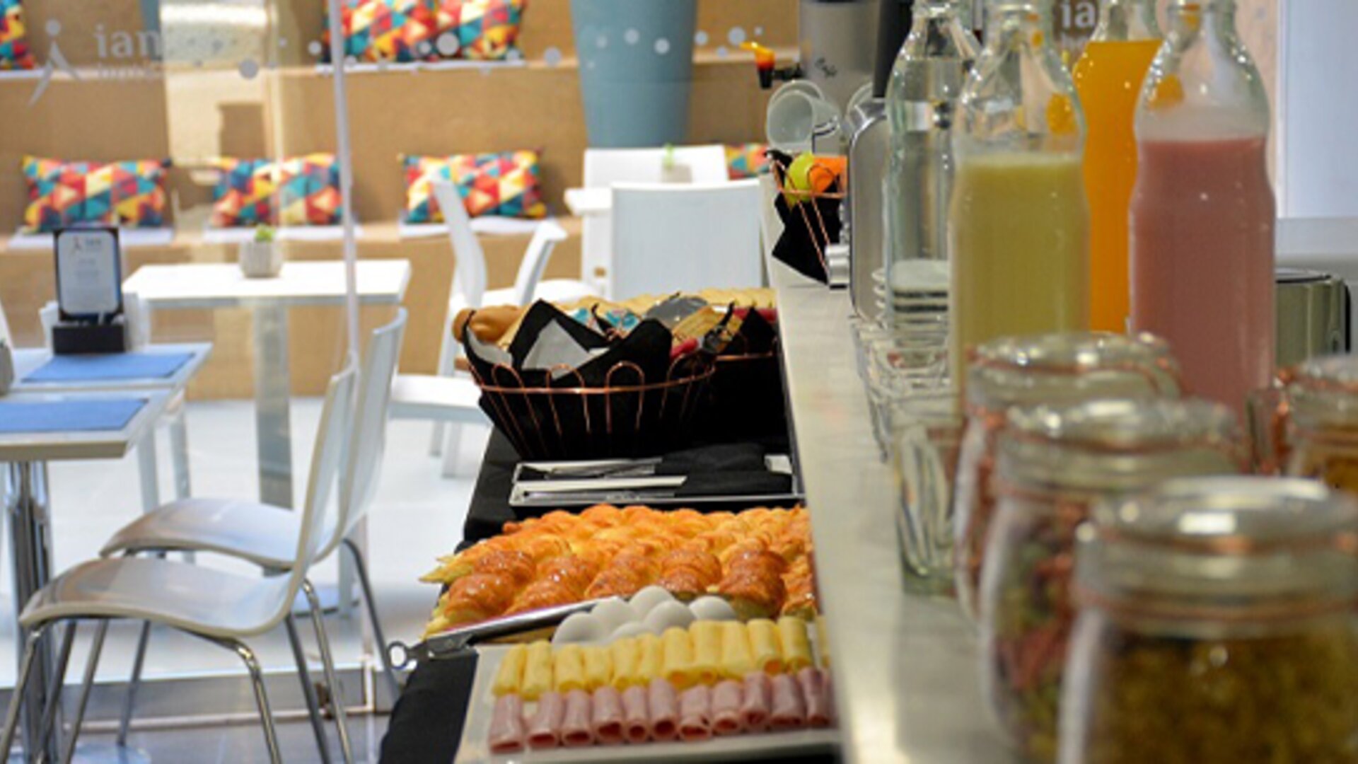 Breakfast buffet with pastries, sliced cold meats, juice bottles and jars of preserves beside dining tables at Ian Hotel.