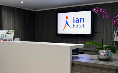 Hotel reception desk with white counter, wall-mounted Ian Hotel logo screen and purple orchids at Ian Hotel.