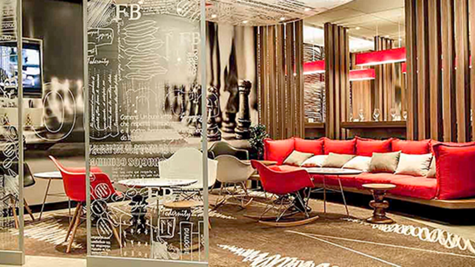 Hotel lobby with red sofas, decorative glass partitions, wooden slat dividers and patterned carpeting at Ibis Lima Reducto Miraflores.