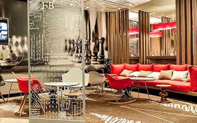 Hotel lobby with red sofas, decorative glass partitions, wooden slat dividers and patterned carpeting at Ibis Lima Reducto Miraflores.