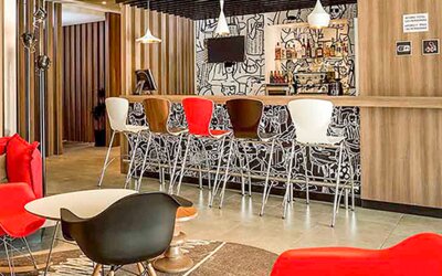 Hotel lounge with red sofas, colorful chairs, round coffee tables and patterned carpet at Ibis Lima Reducto Miraflores.